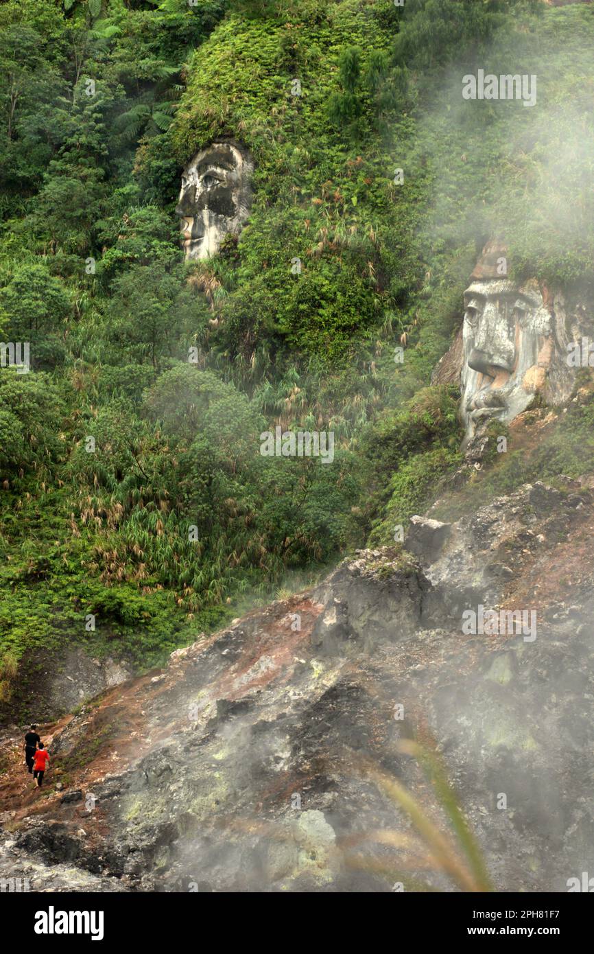 I visitatori stanno camminando sul campo di fumarole per raggiungere formazioni rocciose giganti che illustrano i personaggi di Toar e Lumimuut, gli antenati del popolo Minahasan secondo la mitologia locale, che sono costruiti sul lato di una collina a Bukit Kasih, una destinazione popolare per la cultura, la natura, E il turismo religioso situato nel villaggio di Kanonang, Kawangkoan occidentale, Minahasa, Sulawesi settentrionale, Indonesia. Foto Stock