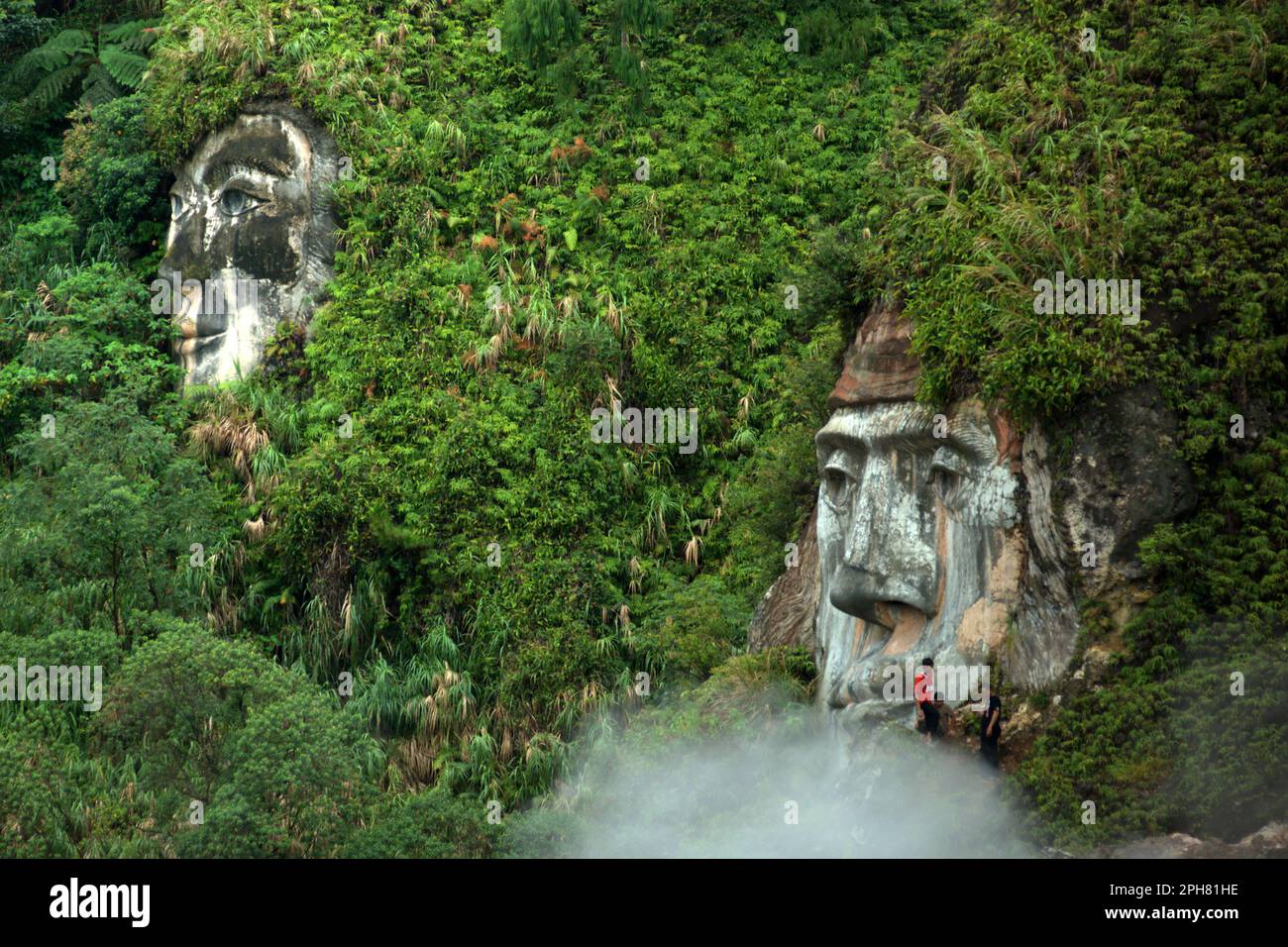 I visitatori hanno tempo libero vicino a una gigantesca formazione del volto che illustra il carattere del Toar, che, insieme a Lumimuut (visto in lontananza) Sono creduti come gli antenati del popolo di Minahasan secondo la mitologia locale, a Bukit Kasih, una destinazione popolare per il turismo culturale, naturale e religioso situato nel villaggio di Kanonang, Kawangkoan occidentale, Minahasa, Sulawesi settentrionale, Indonesia. Foto Stock