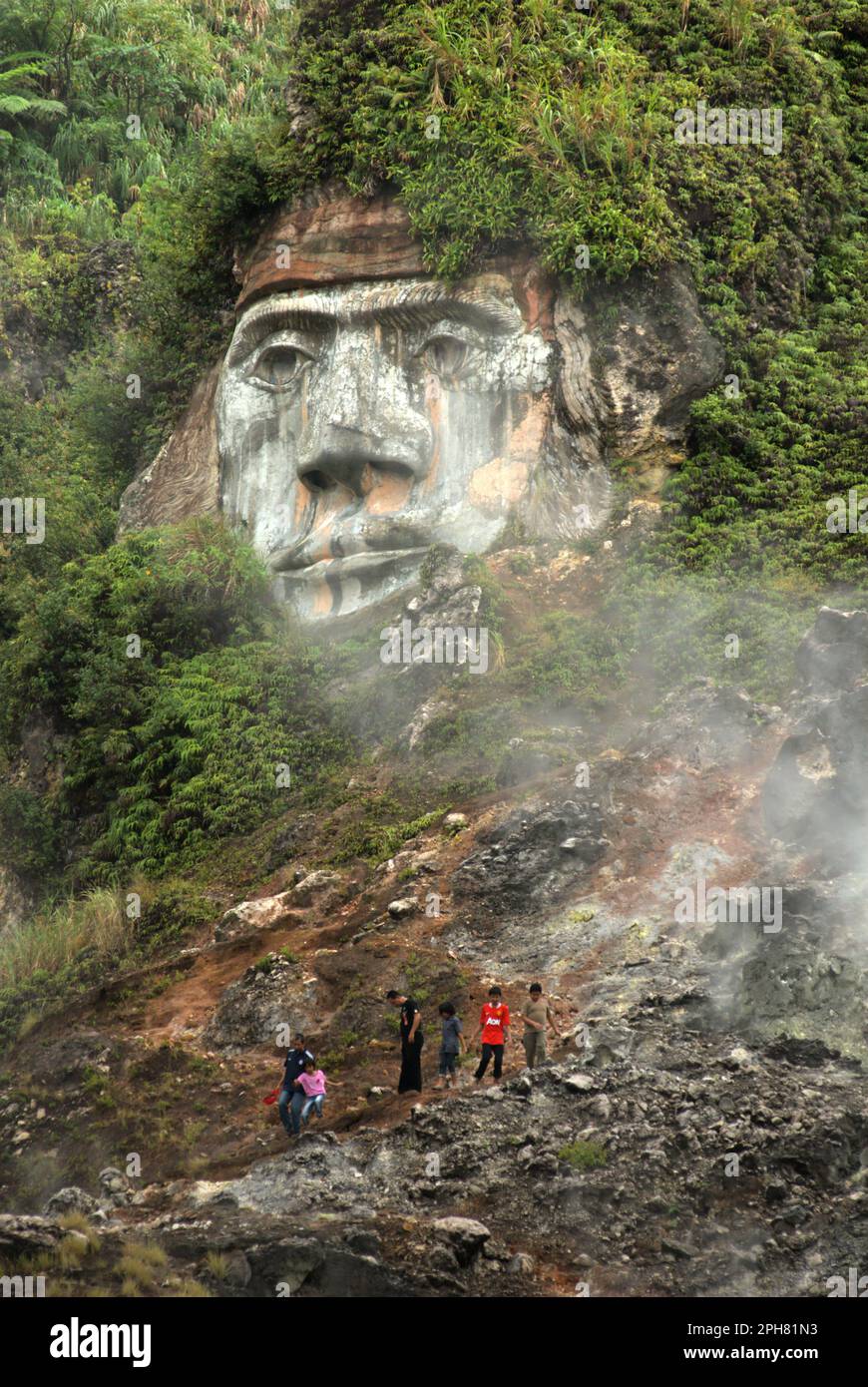 I visitatori hanno tempo libero sul campo delle fumarole, sullo sfondo di una gigantesca formazione facciale che illustra il carattere del Toar, che, insieme a Lumimuut, è Sono creduti come gli antenati del popolo di Minahasan secondo la mitologia locale, a Bukit Kasih, una destinazione popolare per il turismo culturale, naturale e religioso situato nel villaggio di Kanonang, Kawangkoan occidentale, Minahasa, Sulawesi settentrionale, Indonesia. Foto Stock