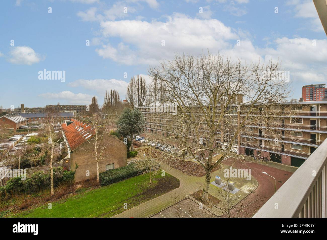 una zona esterna con alberi ed edifici sullo sfondo, presa da un balcone che guarda verso il basso su un albero che non ha foglie Foto Stock