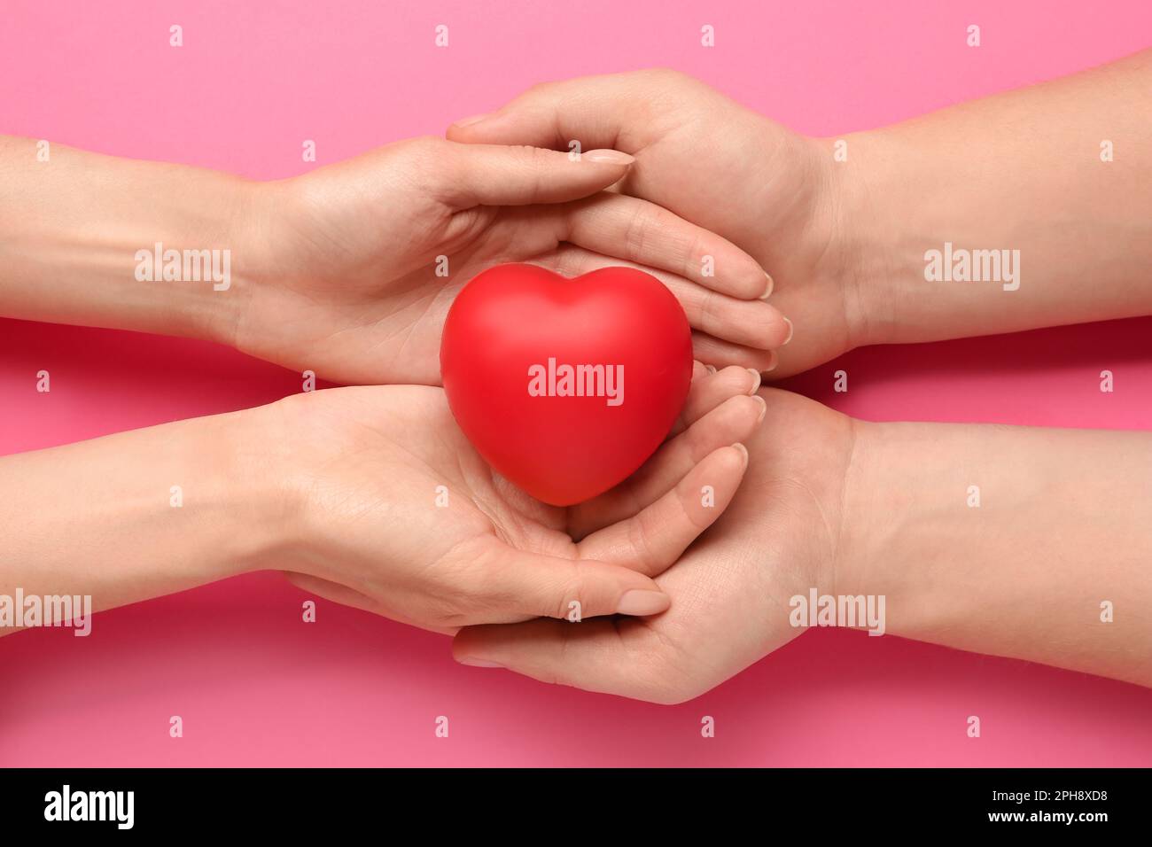 Persone che tengono rosso cuore decorativo su sfondo rosa, vista dall'alto. Concetto di cardiologia Foto Stock