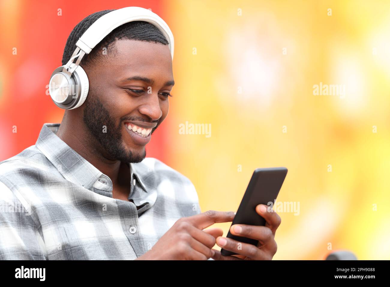 Buon uomo nero che indossa le cuffie per ascoltare la musica sullo smartphone Foto Stock