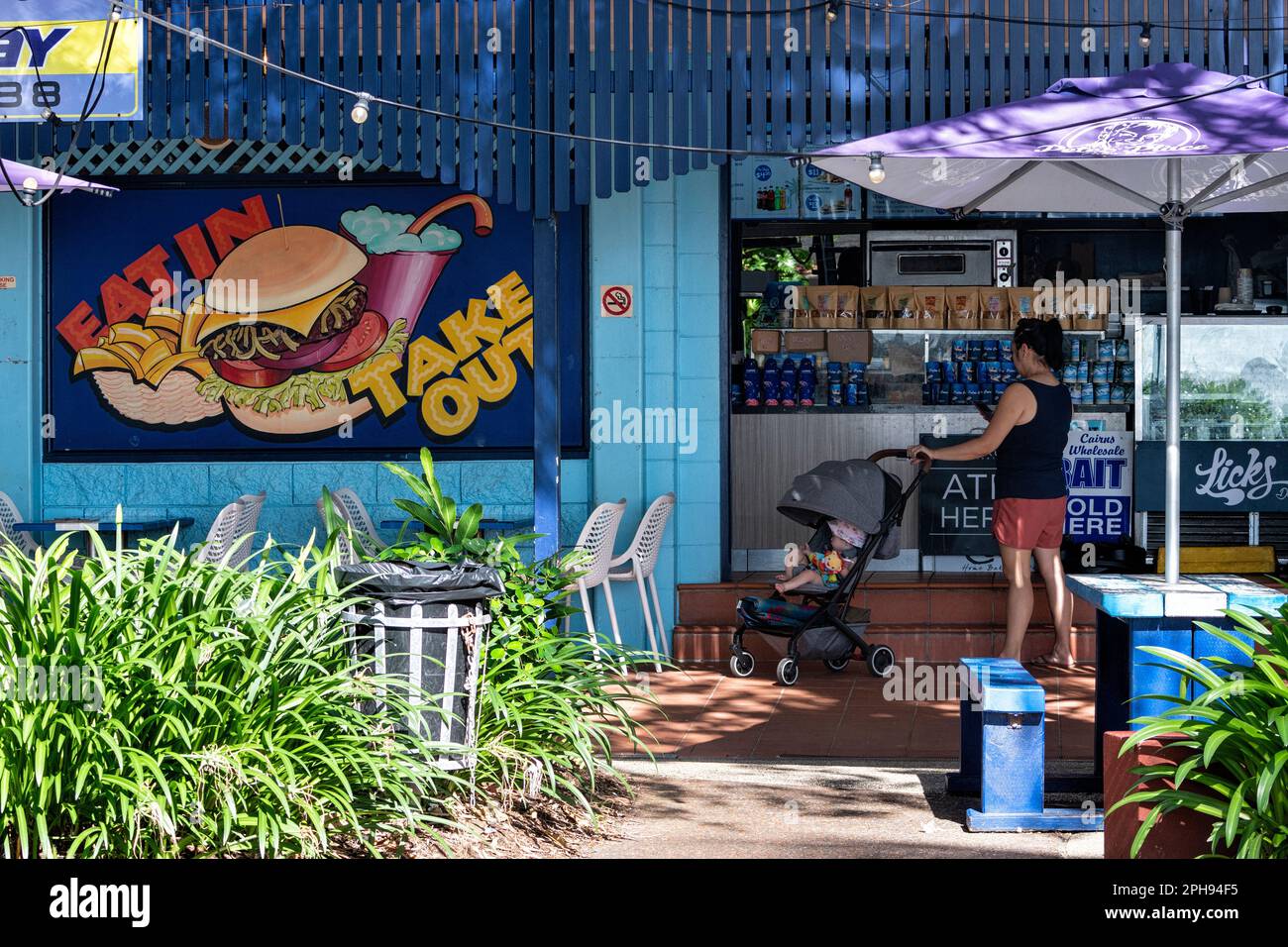 Giovane donna con un gram in attesa di un take away su Palm Cove Esplanade, Cairns Northern Beaches, far North Queensland, FNQ, QLD, Australia Foto Stock