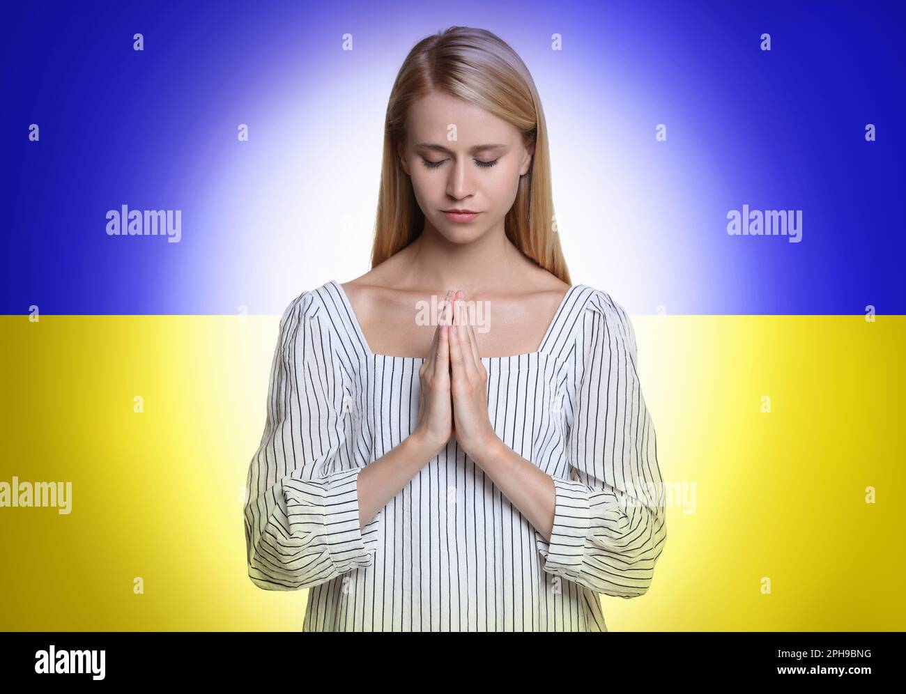 Pregate per l'Ucraina. Giovane donna con mani stringate che prega contro la bandiera nazionale Ucraina Foto Stock