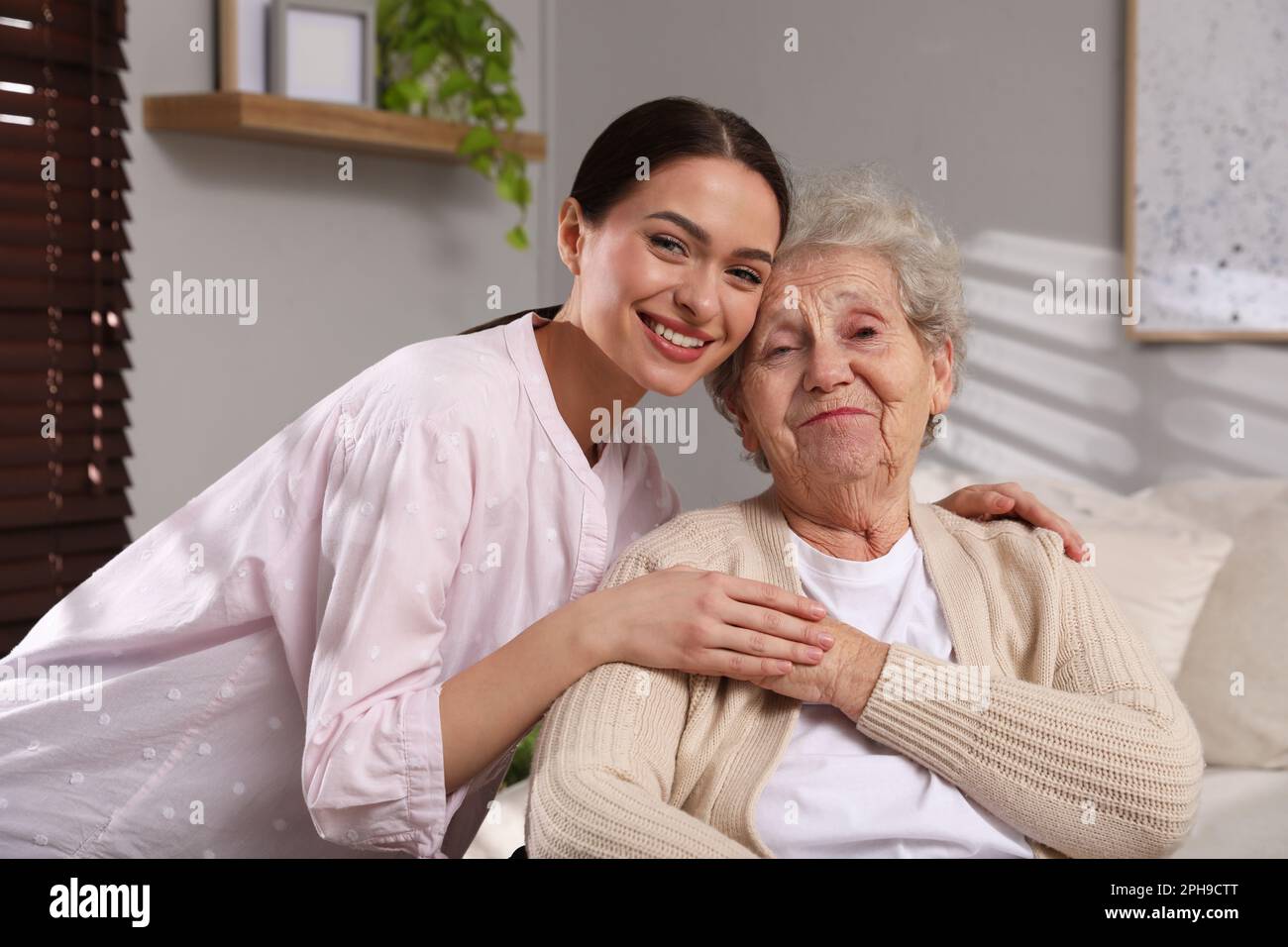 Ritratto di giovane caregiver e donna anziana al chiuso. Assistenza domiciliare Foto Stock