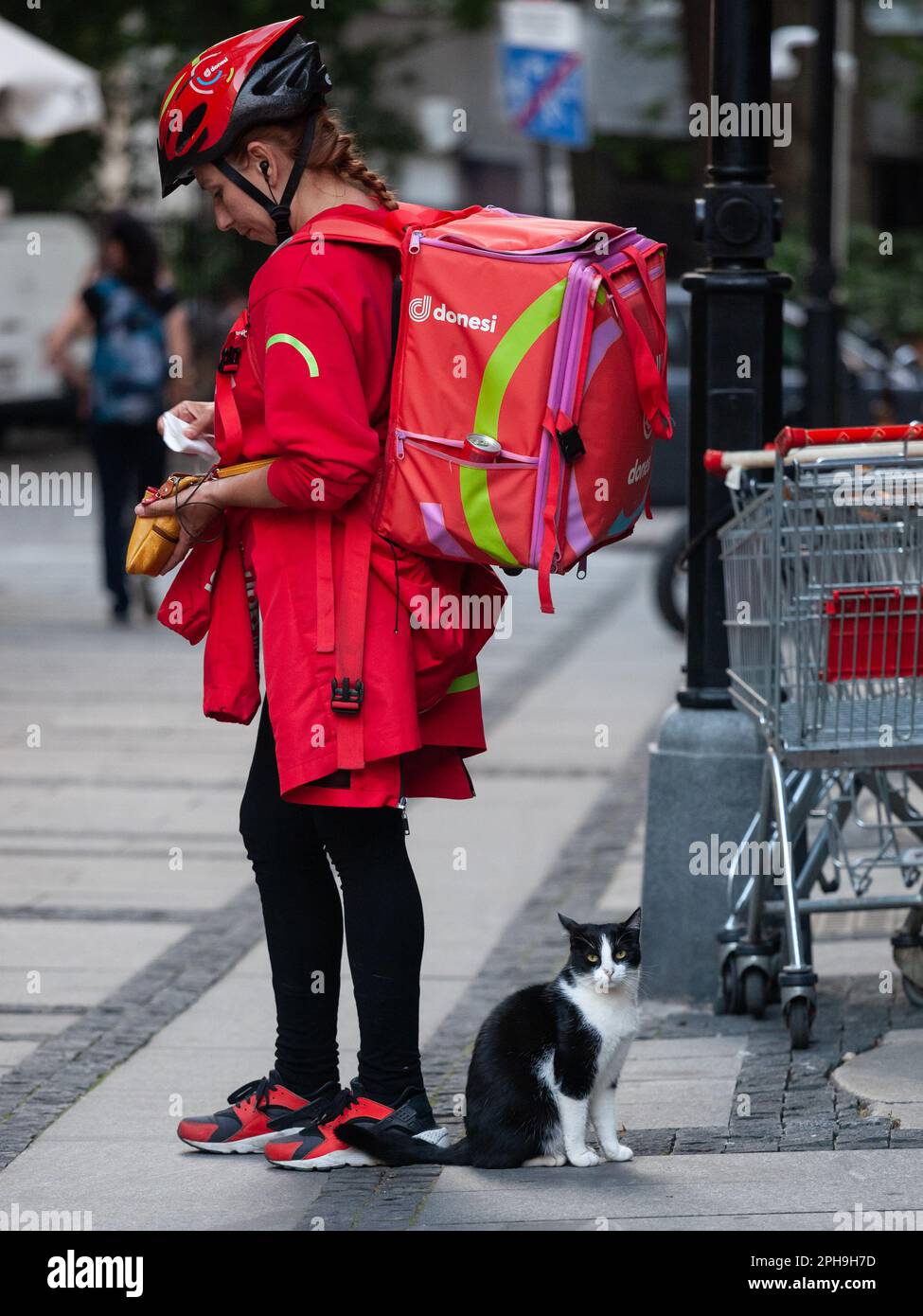 Foto di una ragazza, di una lavoratrice, di un addetto alla consegna, che lavora per l'app di consegna dei prodotti alimentari dalla Serbia Donesi, in piedi per le strade di Belgrado da una via Foto Stock