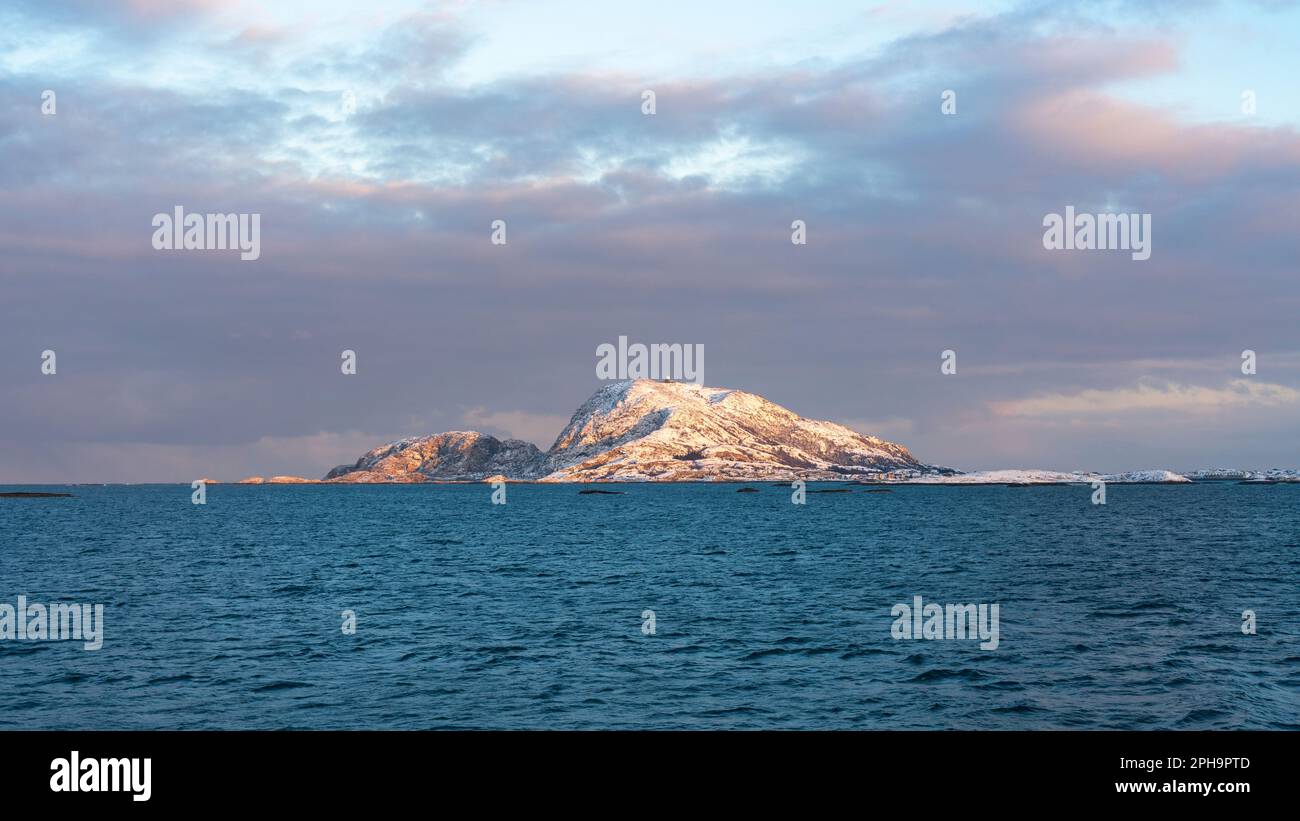 Morgenstimmung auf der Insel Senja und Kvaløya im Winter in Norvegia. Das Morgenrot färbt schneebedeckte Berge und Wolken rötlich, buntes Haus am Ufer Foto Stock