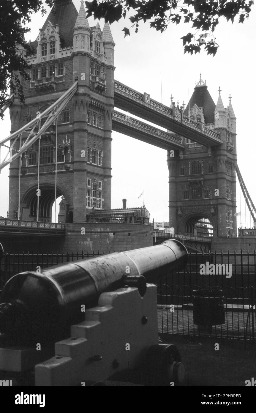 Londra. 1984. Una vista del Tower Bridge presa da Tower Wharf, sulla riva nord del Tamigi a Londra, Inghilterra. In primo piano si trova uno dei vecchi cannoni navali esposti fuori dalla Torre di Londra. Foto Stock