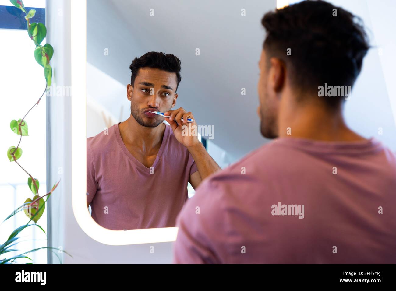 Uomo biraciale che si guarda in specchio e si sfrega i denti in bagno Foto Stock