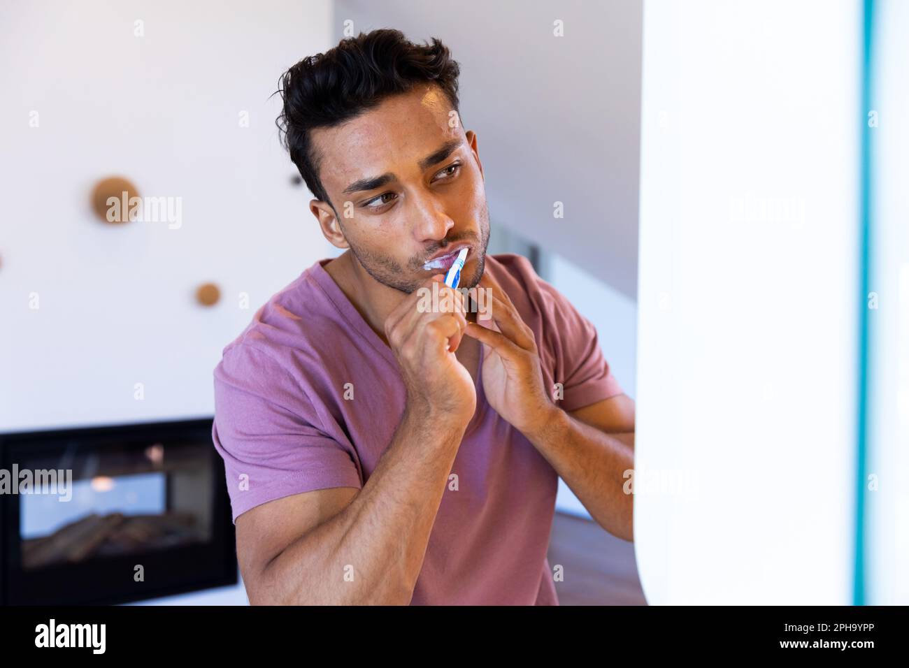 Uomo biraciale che si guarda in specchio e si sfrega i denti in bagno Foto Stock