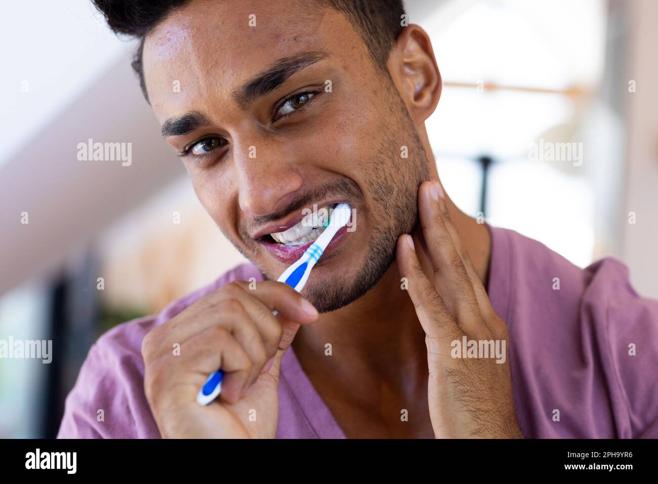 Felice uomo biraciale spazzolando i denti in bagno, sorridendo Foto Stock