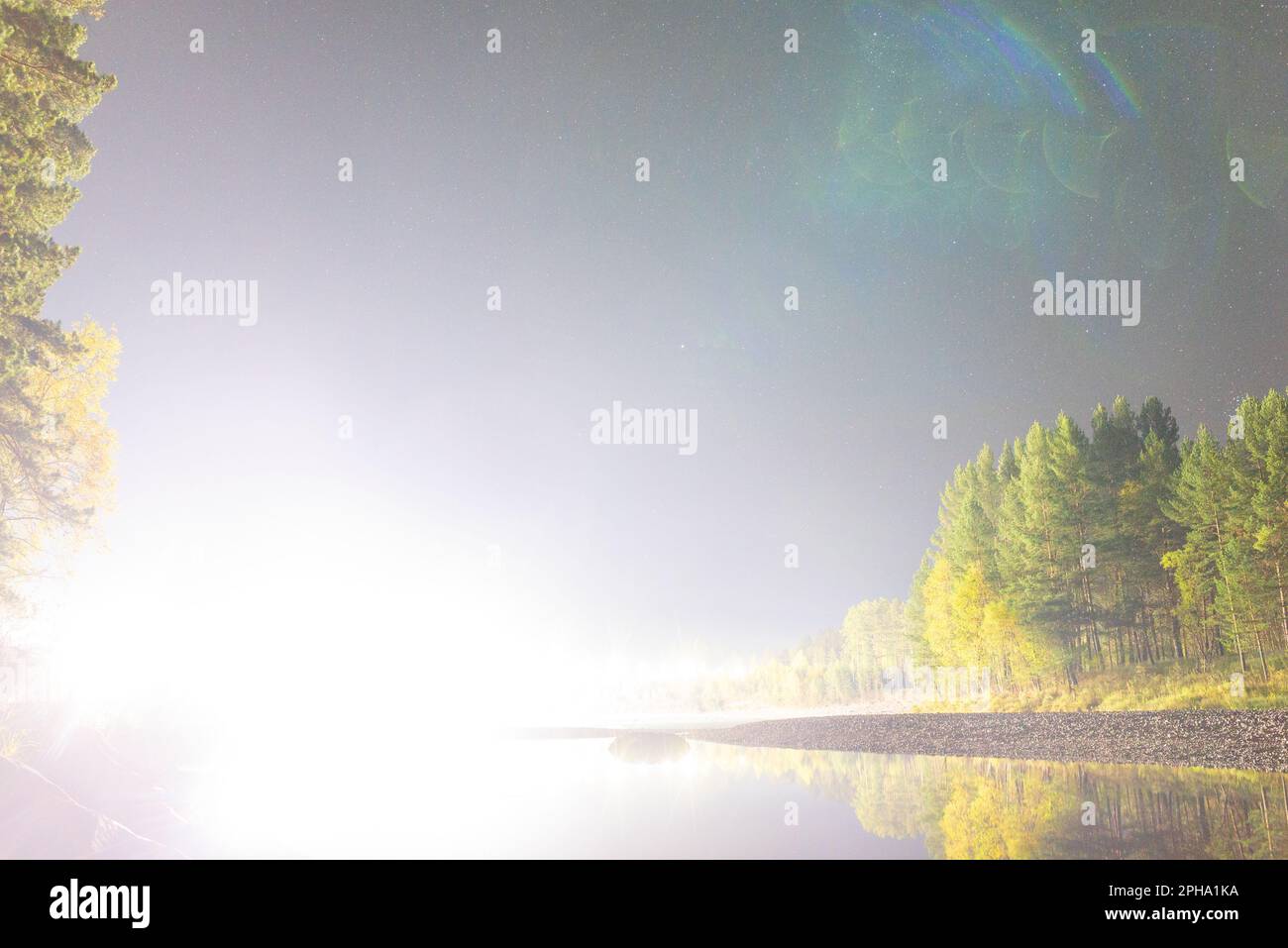 Luce brillante come dall'arrivo della nave UFO sulla riva del fiume con alberi di notte con stelle nelle montagne Altai. Foto Stock