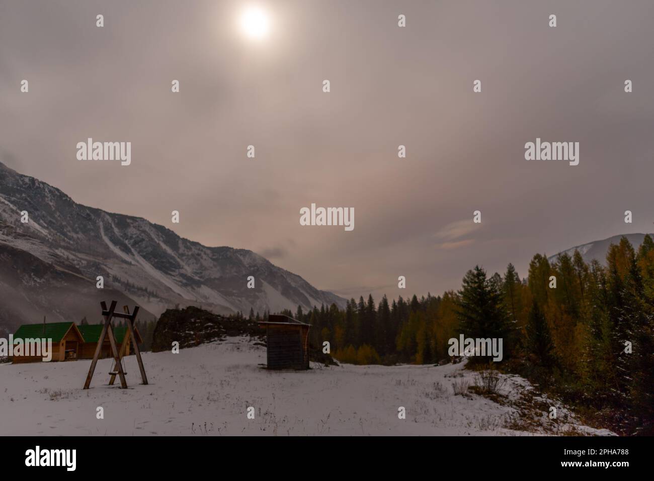 Un altalena in legno vicino alle case vacanze vicino alla foresta sulla neve sotto la montagna con nebbia e neve bianca, con la luce della luna su un luminoso Foto Stock