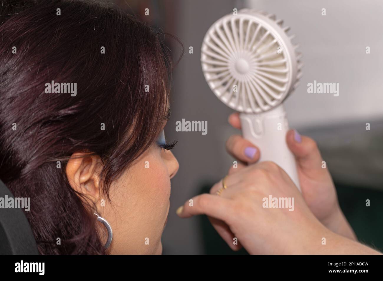 Giovane donna in un salone di bellezza che riceve aria da un piccolo ventilatore per asciugare le sue false ciglia Foto Stock