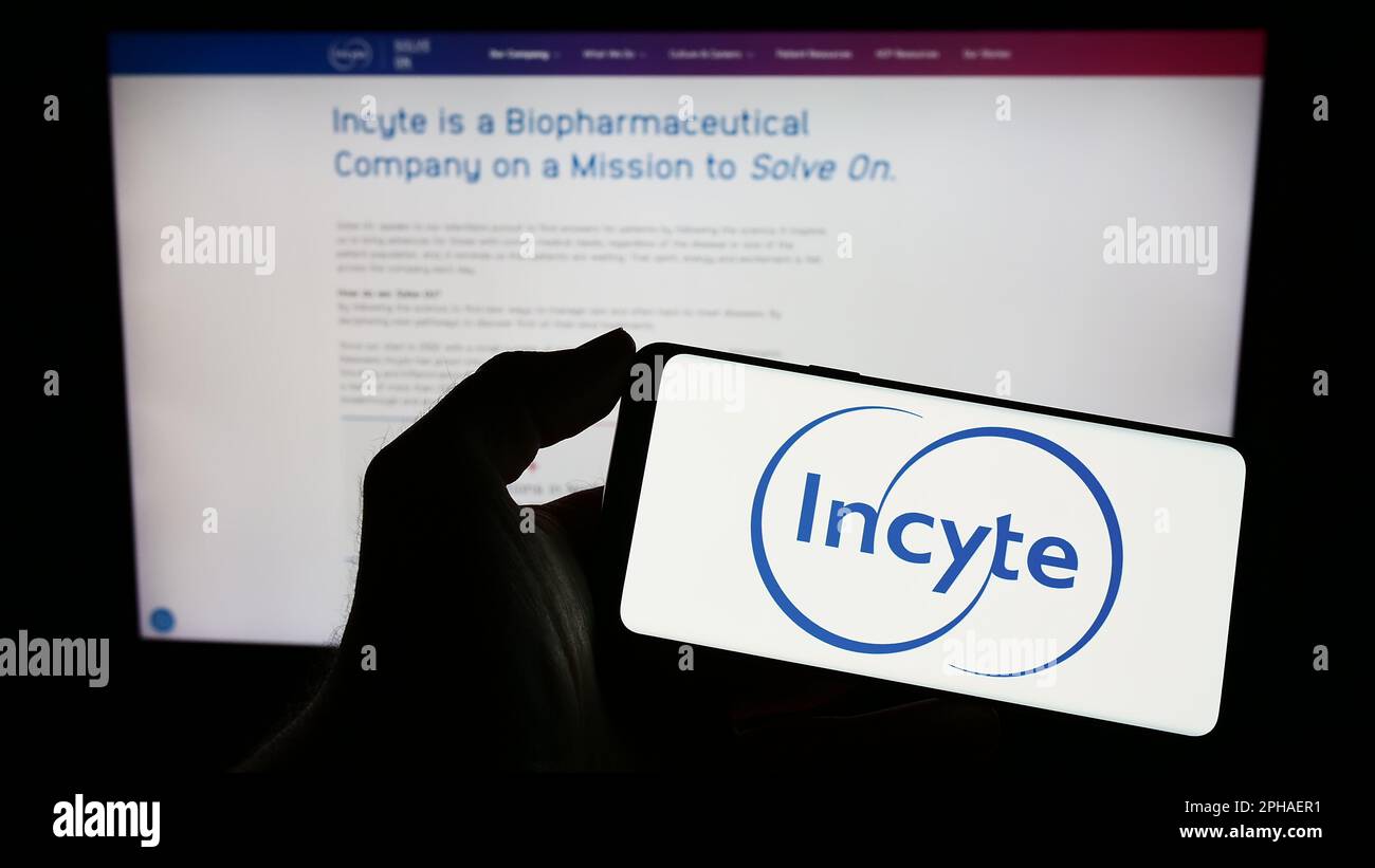 Persona che tiene uno smartphone con il logo della società farmaceutica statunitense Incyte Corporation sullo schermo di fronte al sito Web. Messa a fuoco sul display del telefono. Foto Stock