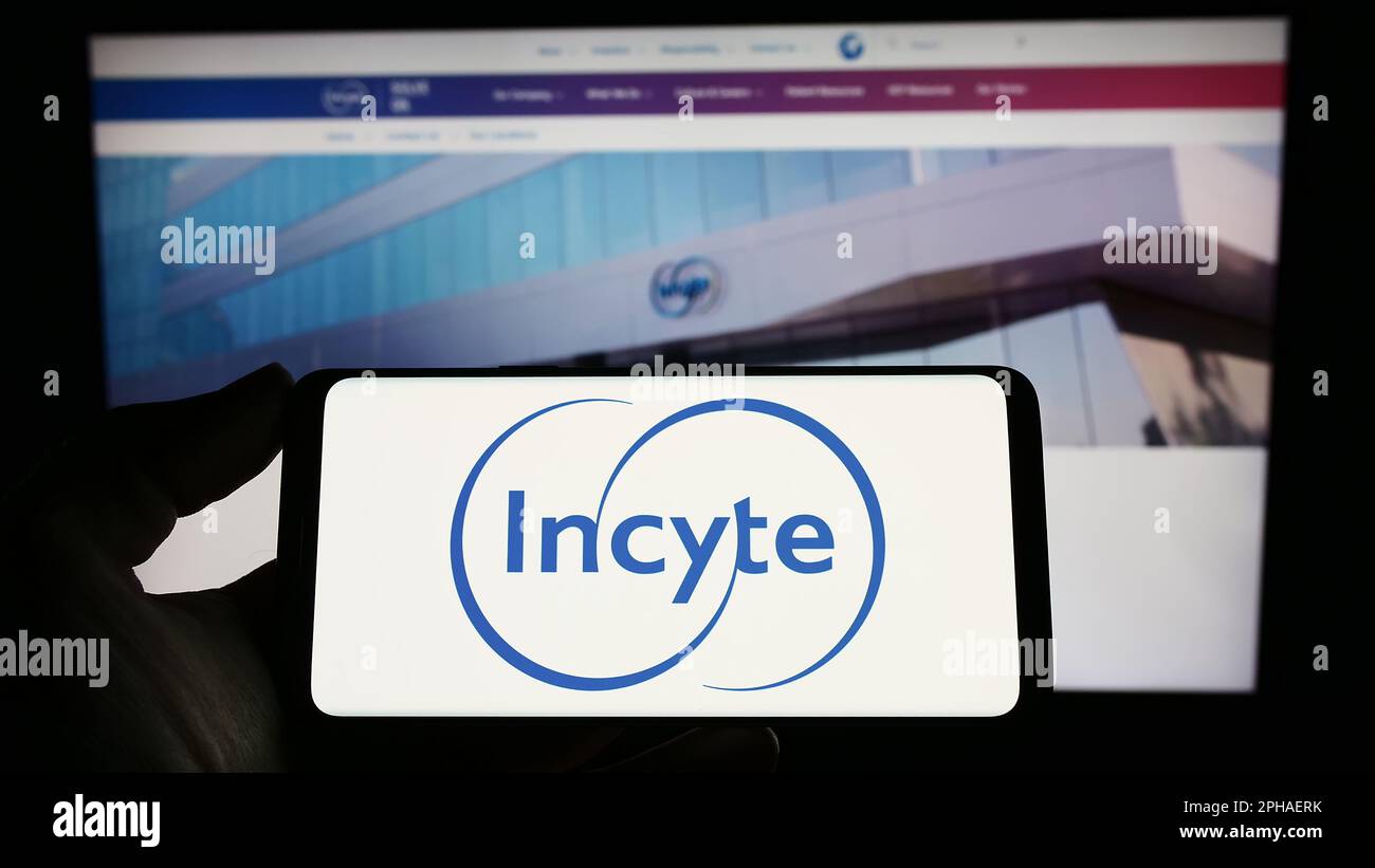Persona che tiene il cellulare con il logo della società farmaceutica americana Incyte Corporation sullo schermo di fronte alla pagina web. Messa a fuoco sul display del telefono. Foto Stock