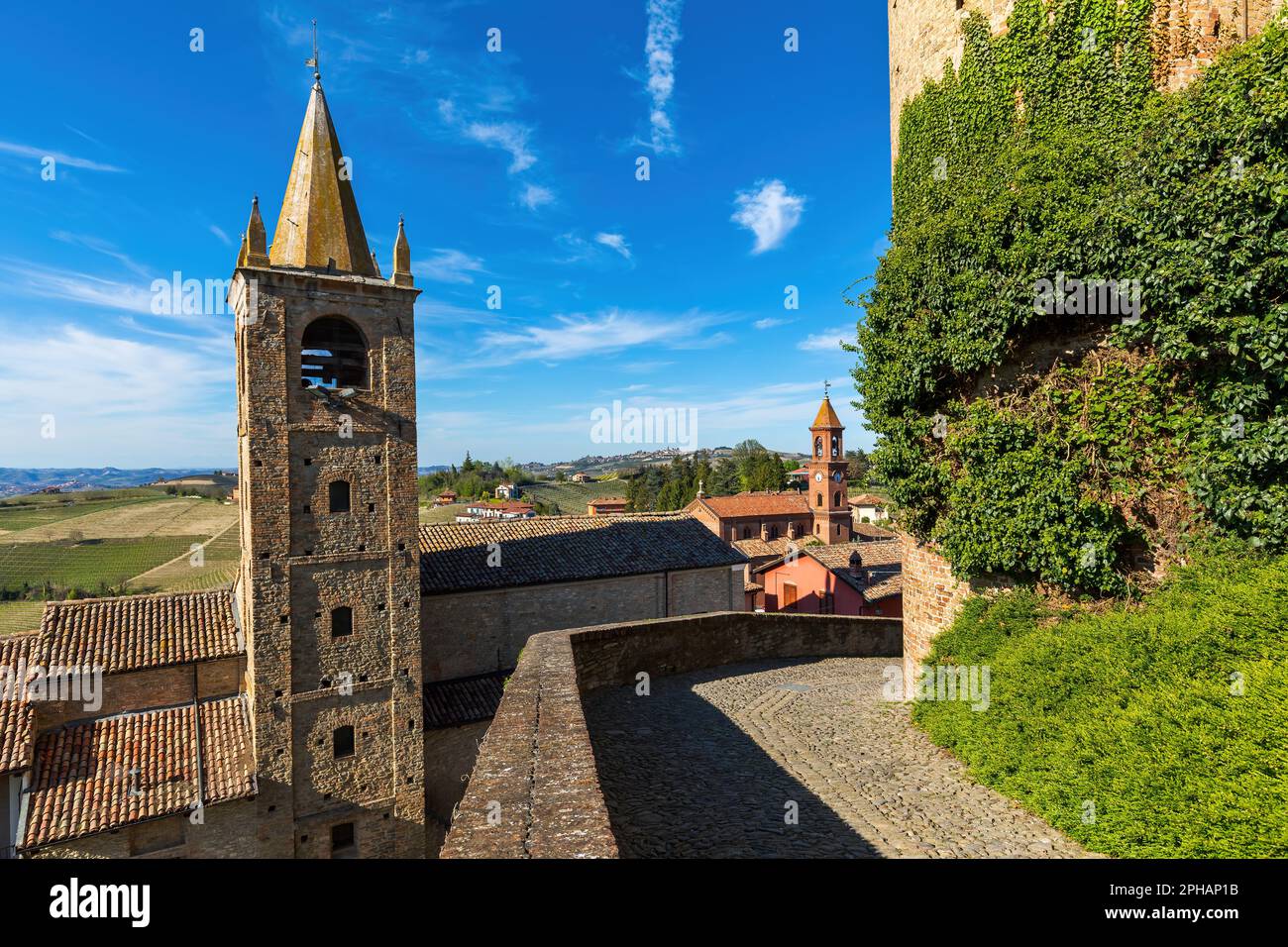 Vista della stretta strada acciottolata, dei tetti e del vecchio campanile medievale sotto il cielo blu nella piccola città di Serralunga d'Alba, Italia. Foto Stock