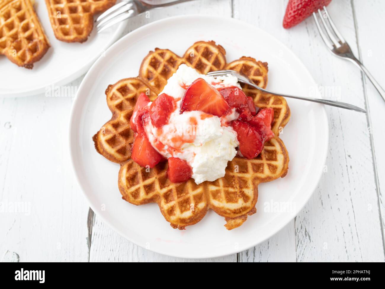 Waffle con panna montata e guarnizione di fragola su un piatto dall'alto Foto Stock