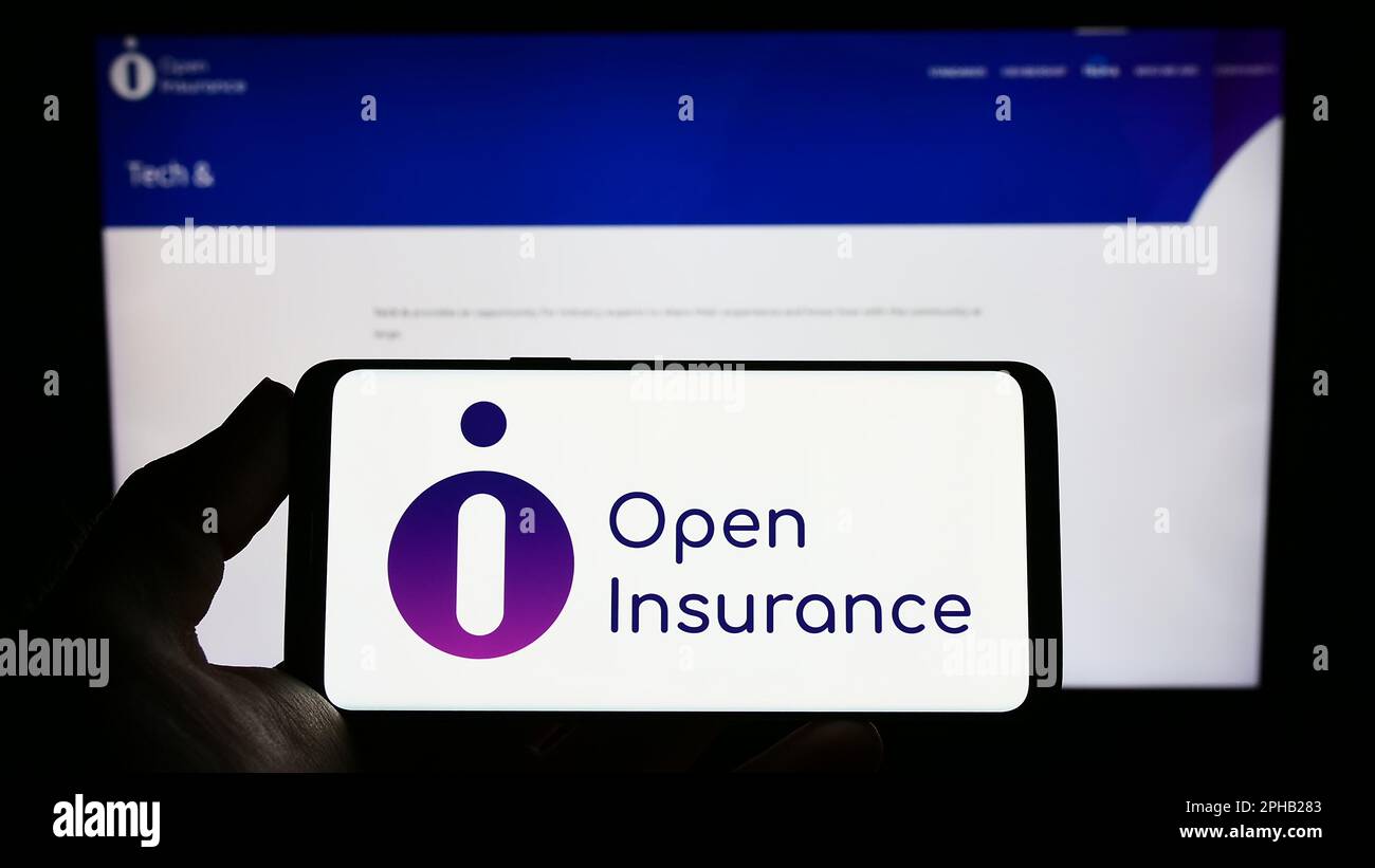 Persona che tiene il telefono cellulare con il logo di iniziativa del settore Open Insurance sullo schermo di fronte alla pagina web. Messa a fuoco sul display del telefono. Foto Stock