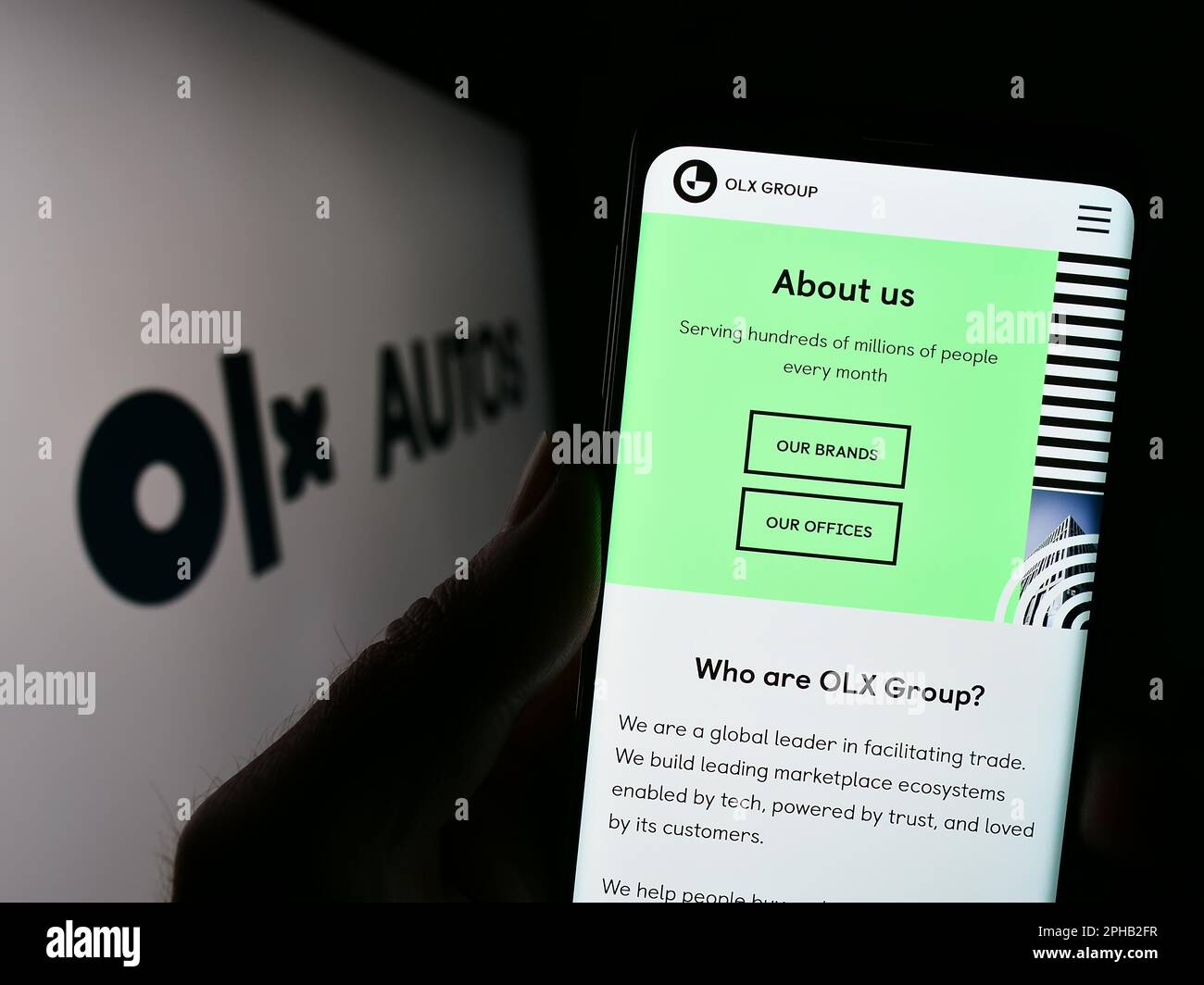 Persona in possesso di smartphone con il sito web della società olandese di commercio di automobili OLX Global B.V. sullo schermo di fronte al logo. Messa a fuoco al centro del display del telefono. Foto Stock