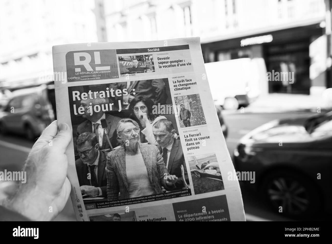 Parigi, Francia - Mar 20, 2023: Immagine monocromatica - POV maschio mano acquistare stampa leggere le repubblicano Lorrain con Elisabeth Borne e voti riforma pensionistica voluto dal governo francese che avrebbe innalzato l'età pensionabile da 62 a 64 Foto Stock