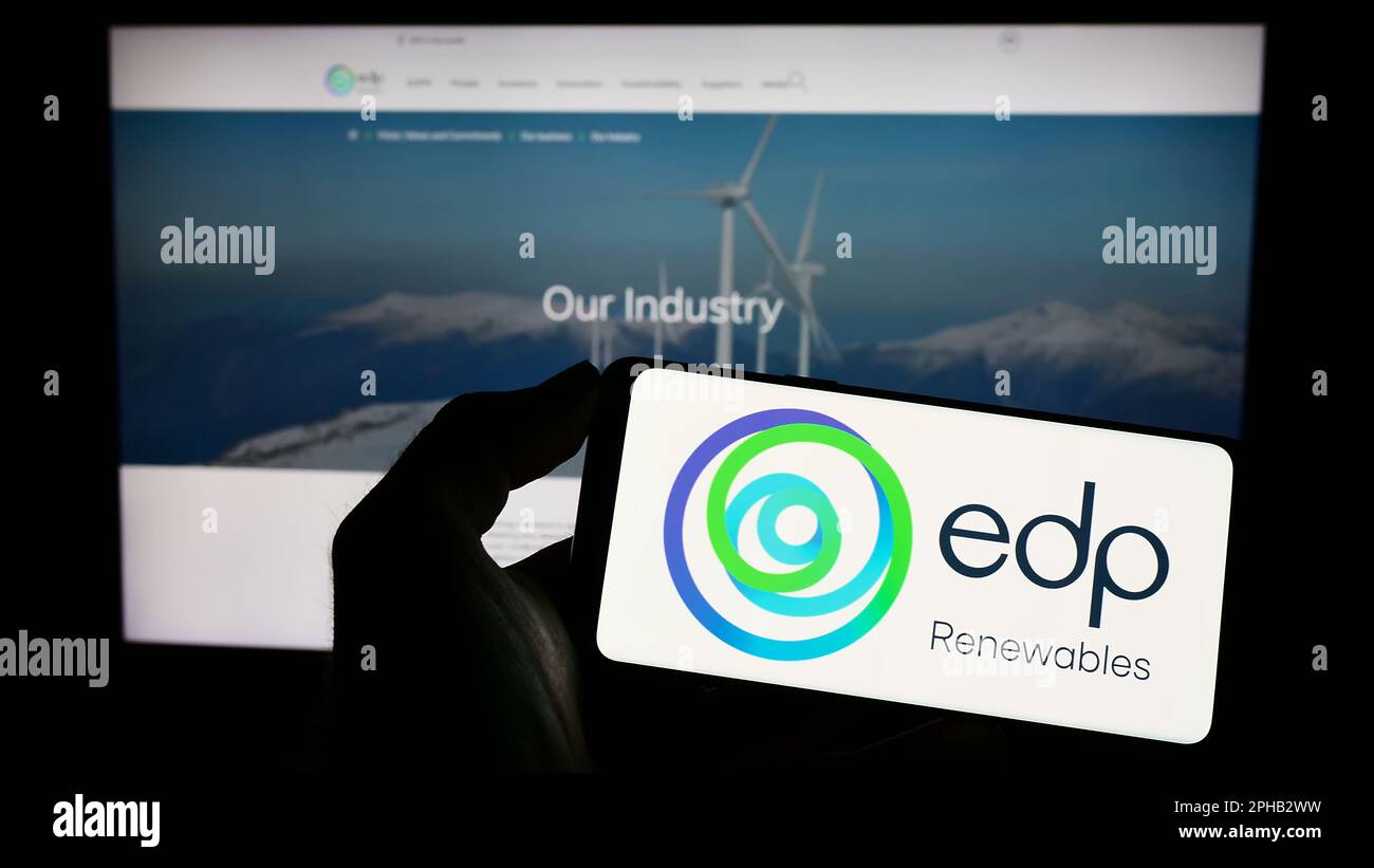 Persona che detiene uno smartphone con il logo della società spagnola EDP Renovaveis S.A. per l'energia (EDPR) sullo schermo davanti al sito Web. Messa a fuoco sul display del telefono. Foto Stock