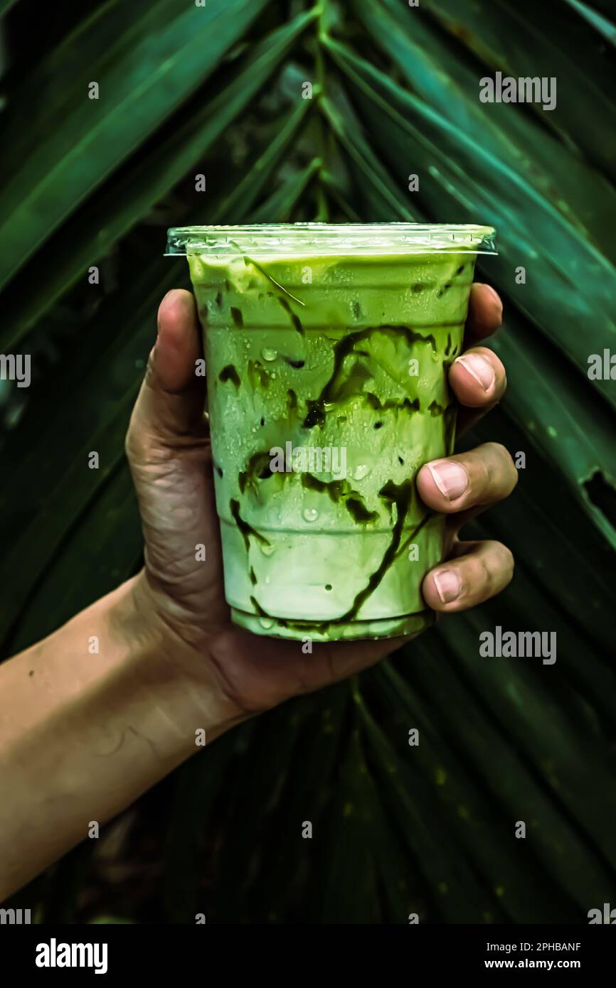 Tè ghiacciato verde matcha mescolato con cubetto di ghiaccio e latte in vetro latte con sfondo verde natura Foto Stock