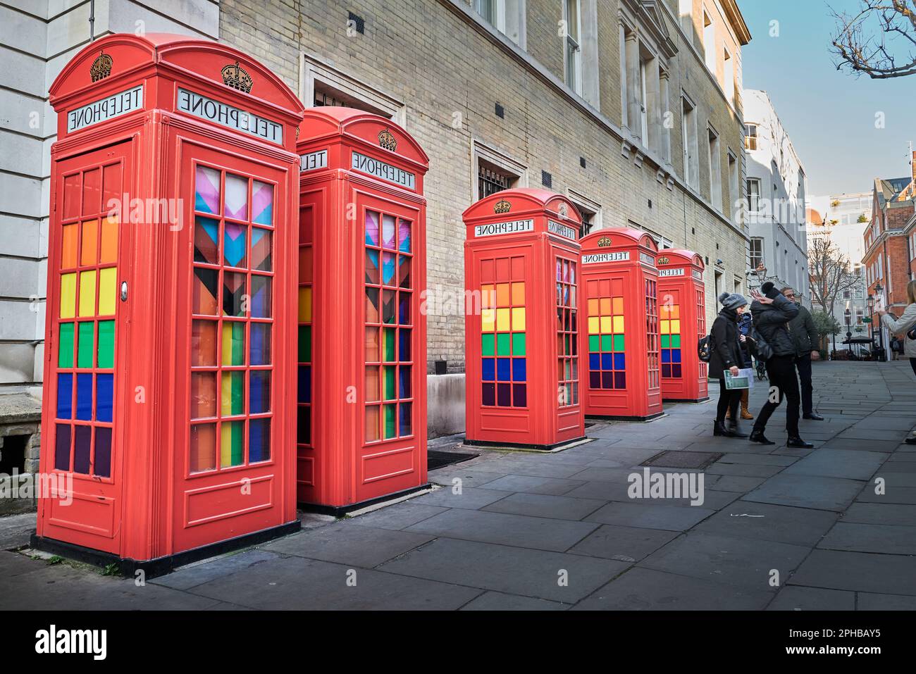 Turisti accanto a cabine telefoniche rosse adornate con i colori LGBTQ, Londra, Inghilterra. Foto Stock