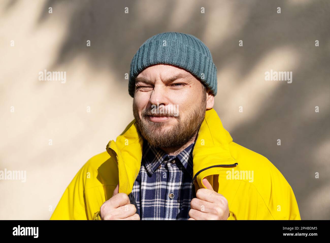 Ritratto dell'uomo bearded che indossa giacca gialla d'inverno e cappello godendo di calde luci del sole di primavera. Foto Stock