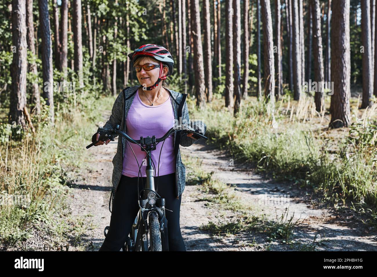 Donna attiva in bicicletta su strada forestale. Donna in bicicletta in fuoristrada percorso durante il giorno delle vacanze estive. Donna che indossa casco e guanti da bicicletta Foto Stock