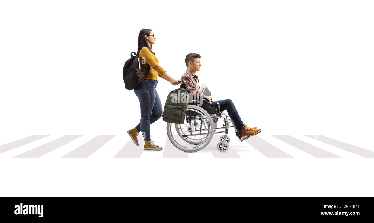 Profilo a tutta lunghezza di una studentessa che spinge un amico su una sedia a rotelle in un passaggio pedonale isolato su sfondo bianco Foto Stock