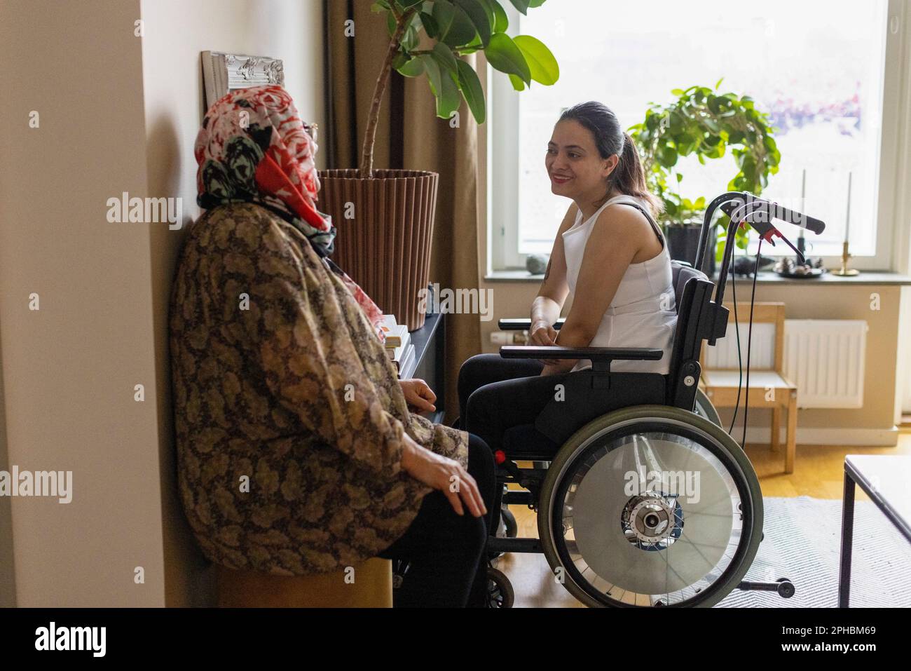 Vista laterale di una donna con paraplegia che parla con la madre a casa Foto Stock