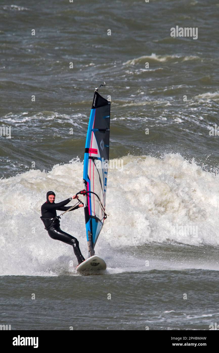 Windsurf ricreativo in muta nera praticando il windsurf classico lungo la costa del Mare del Nord in condizioni di vento durante la tempesta invernale Foto Stock