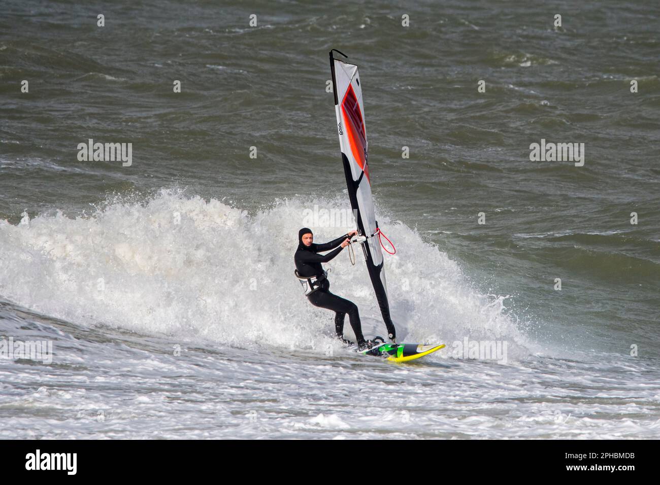 Windsurf ricreativo in muta nera praticando il windsurf classico lungo la costa del Mare del Nord in condizioni di vento durante la tempesta invernale Foto Stock