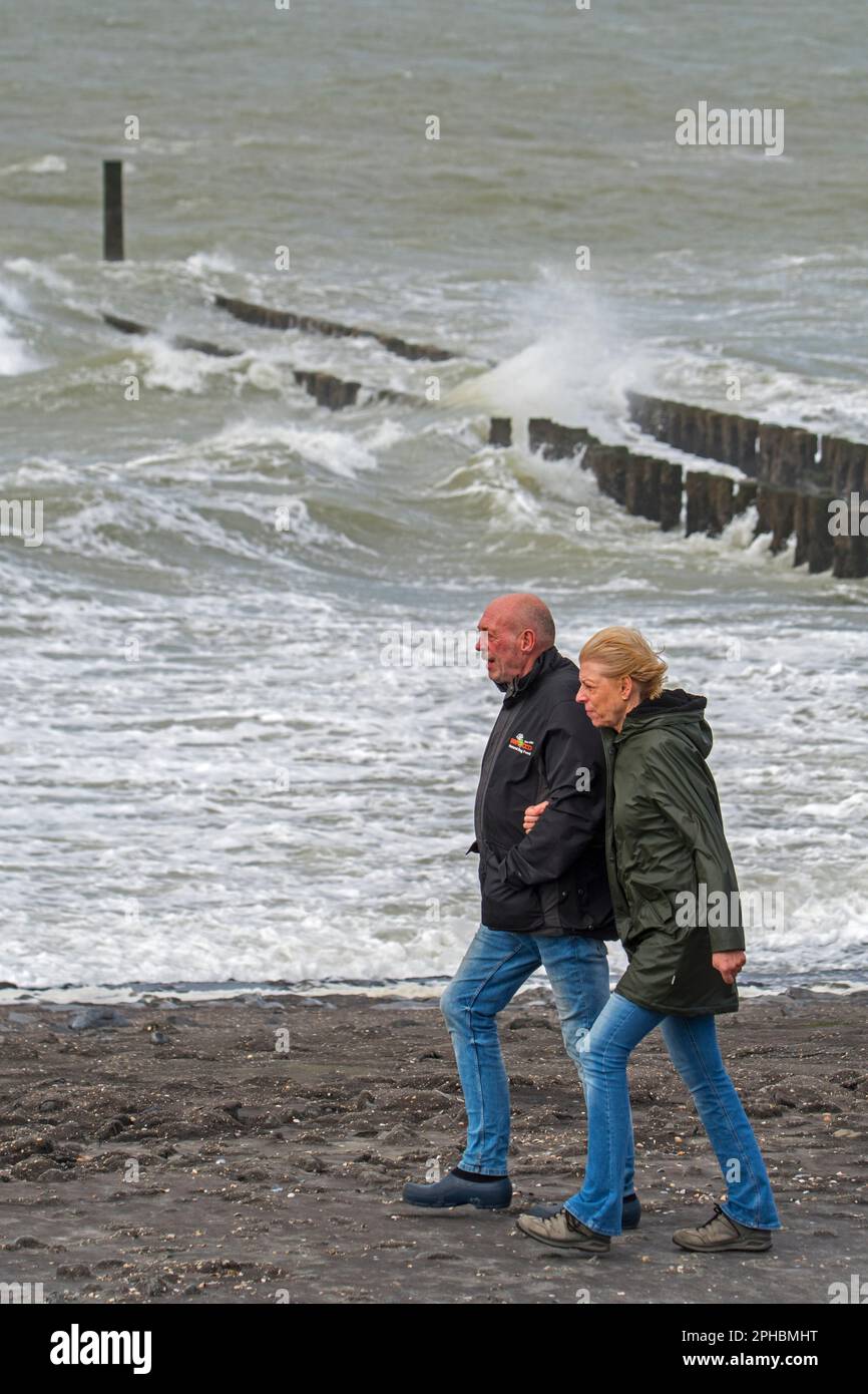 Coppie anziane che camminano lungo la costa del Mare del Nord in una giornata ventosa durante la tempesta invernale in Zeeland, Paesi Bassi Foto Stock