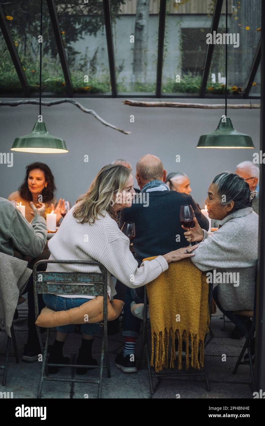 Donna anziana seduta sulla sedia mentre si parla con un'amica in pensione durante la festa a cena Foto Stock