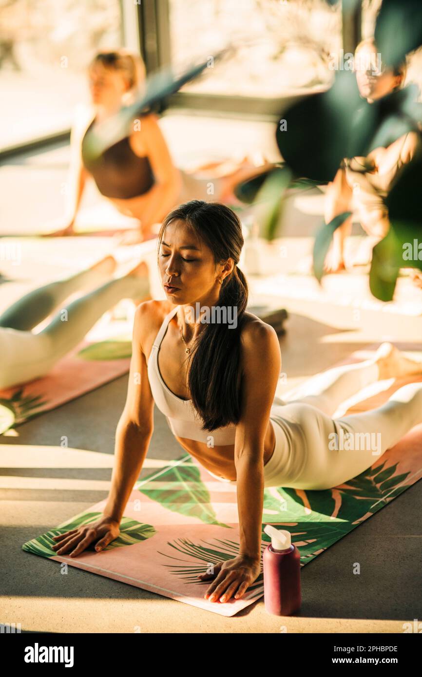 Giovane donna che fa il cobra stretch sul materassino di esercitazione durante la lezione di yoga al centro di ritiro Foto Stock