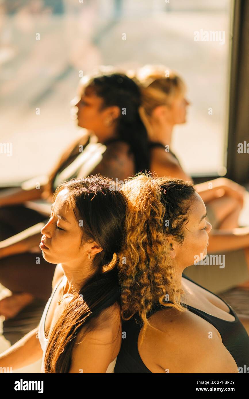 Donne amici seduti a schiena e allenarsi durante la lezione di yoga Foto Stock