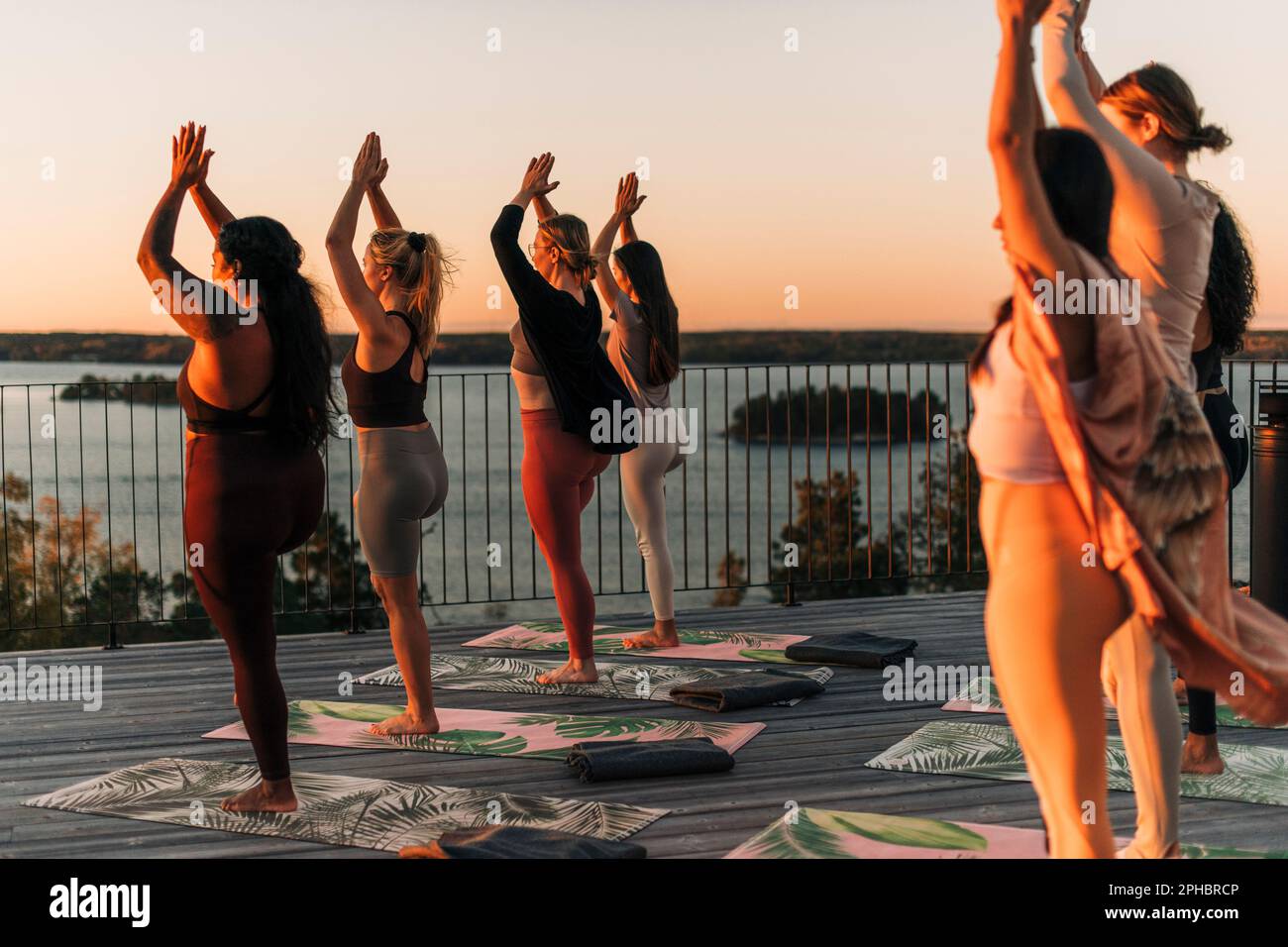 Le amiche che praticano l'albero si posano insieme sul patio al tramonto Foto Stock