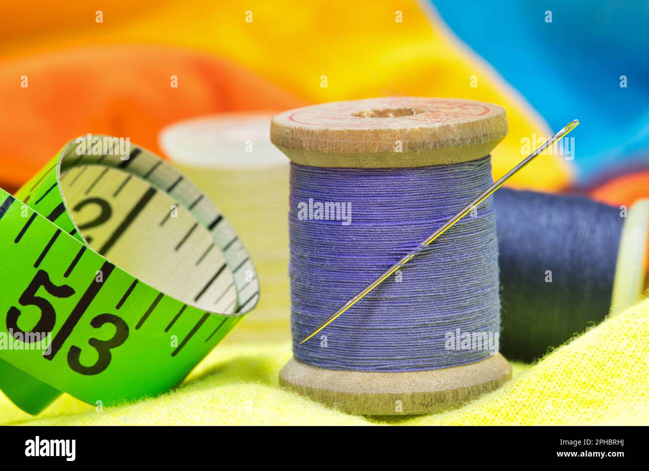 Utensili per cucire isolati su indumenti colorati con macro dettagli tra cui spole di filo, ago e metro a nastro. Foto Stock
