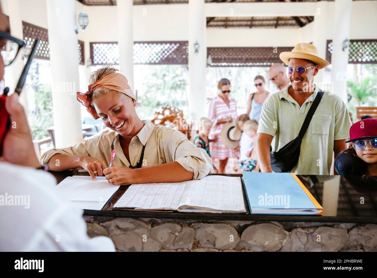 Donna felice che firma alla reception durante il check-in con la famiglia al resort Foto Stock