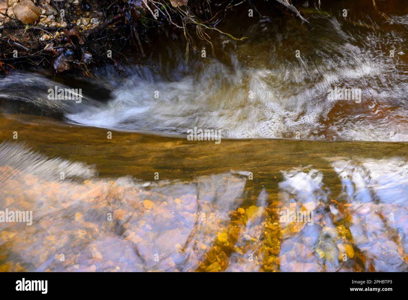 Acqua che scorre velocemente in un flusso che scorre sopra un log, movimento sfocato Foto Stock