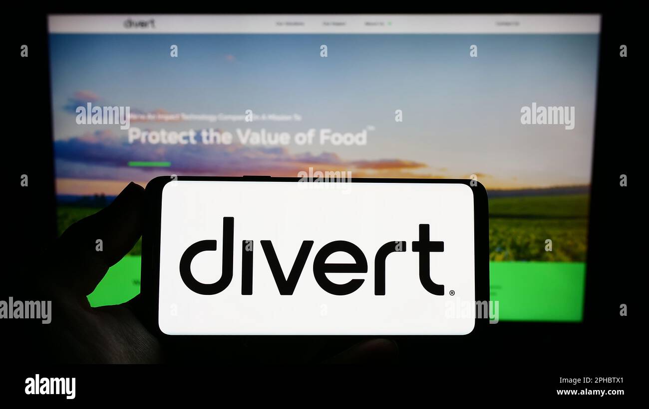 Persona che tiene uno smartphone con il logo della società statunitense di tecnologia alimentare Divert Inc. Sullo schermo di fronte al sito Web. Messa a fuoco sul display del telefono. Foto Stock