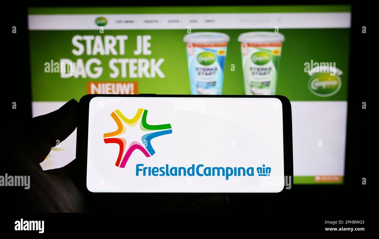 Persona in possesso di smartphone con il logo della società Koninklijke FrieslandCampina N.V. sullo schermo di fronte al sito web. Messa a fuoco sul display del telefono. Foto Stock