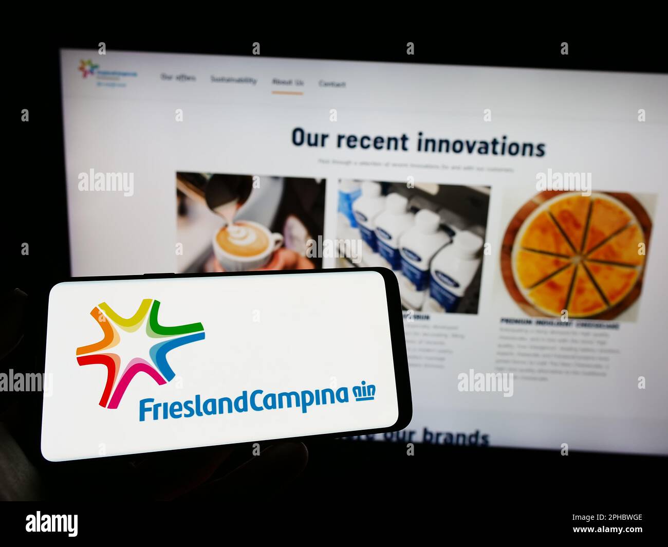 Persona che tiene il cellulare con il logo della società Koninklijke FrieslandCampina N.V. sullo schermo di fronte al sito web aziendale. Messa a fuoco sul display del telefono. Foto Stock