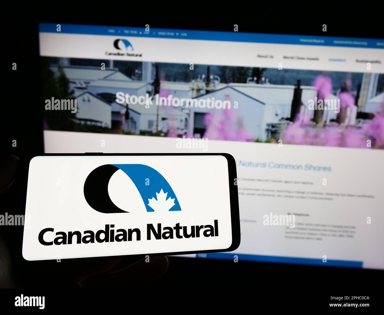 Persona che tiene il telefono cellulare con il logo della società Canadian Natural Resources Limited sullo schermo di fronte alla pagina web. Messa a fuoco sul display del telefono. Foto Stock
