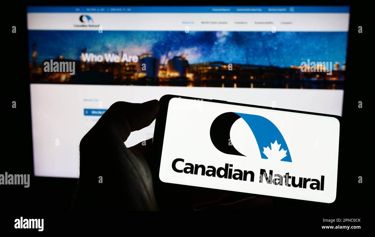 Persona che tiene uno smartphone con il logo della società Canadian Natural Resources Limited sullo schermo davanti al sito Web. Messa a fuoco sul display del telefono. Foto Stock