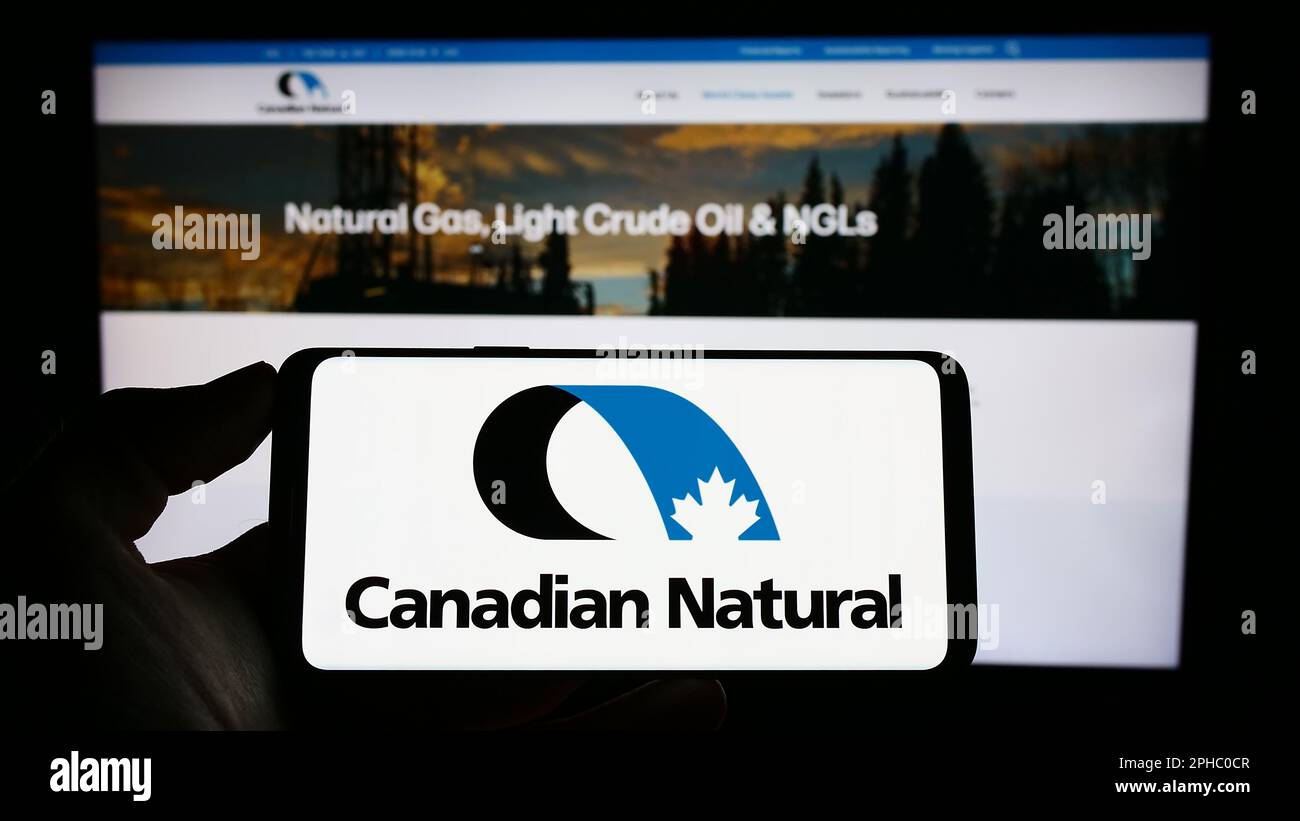 Persona che tiene il cellulare con il logo della società Canadian Natural Resources Limited sullo schermo di fronte al sito web aziendale. Messa a fuoco sul display del telefono. Foto Stock
