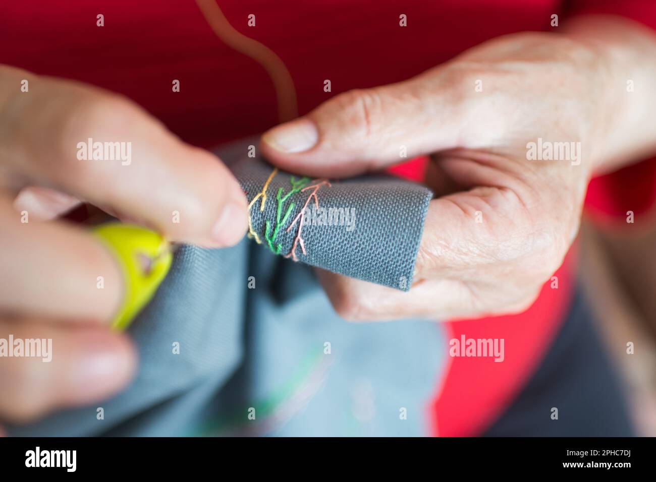 Primo piano delle mani di donna anziana cucire a casa. Tamburo giallo Foto Stock