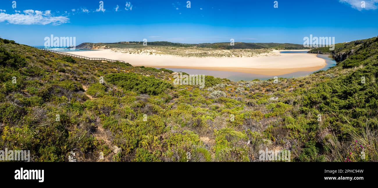 Panorama ultra grandangolare del fiume Ribeira de Aljezur che serpeggia attraverso la sabbia dorata della spiaggia di Praia da Amoreira con acque cristalline e tranquille. Foto Stock